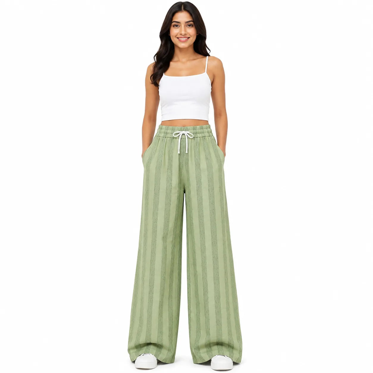 A woman modeling a pair of wide-leg, light sage green pants with vertical stripes and a white drawstring waist, paired with a white crop top and white sneakers, against a solid white background.