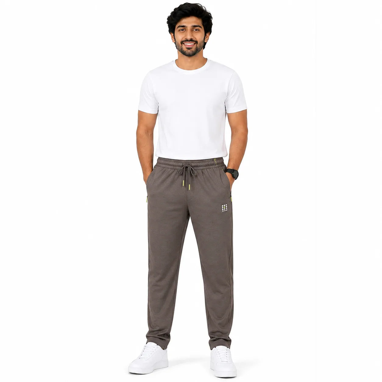 A man modeling a pair of dark brown sweatpants with a white t-shirt and white sneakers, standing against a solid white background.