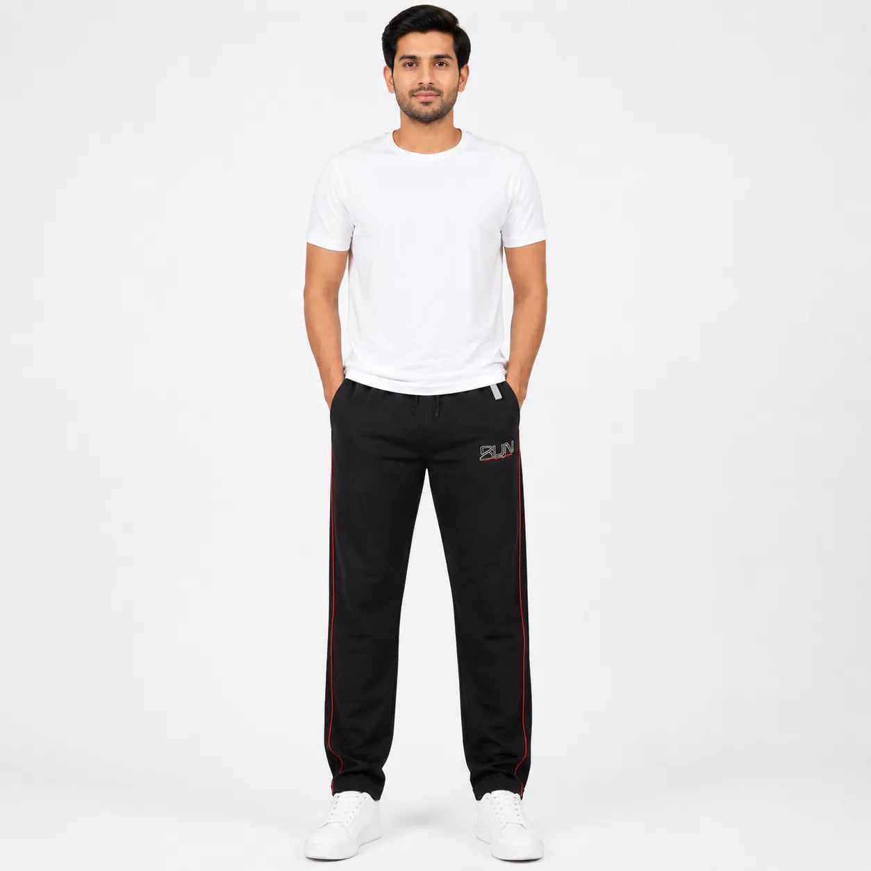 A man modeling black track pants with red side stripes and a small white logo, paired with a white t-shirt and white sneakers, against a plain white studio background.
