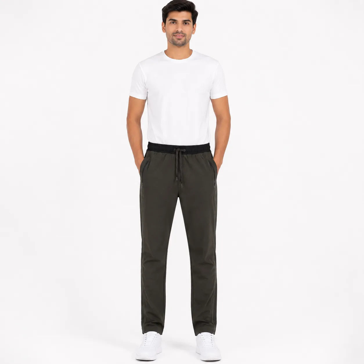 A man modeling dark olive green drawstring pants with a white t-shirt and white sneakers, standing against a plain white studio background.