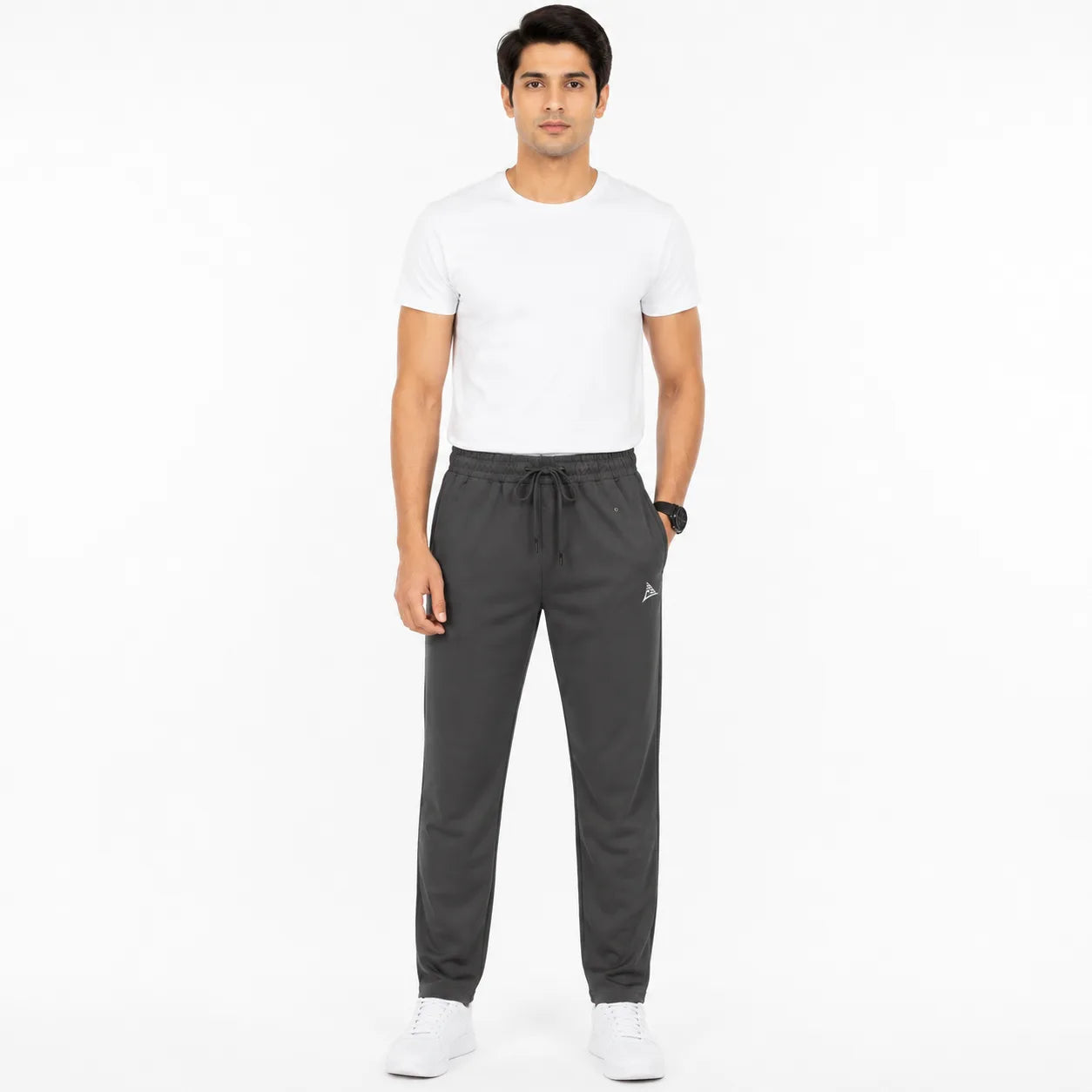 A man modeling dark gray drawstring sweatpants with a white t-shirt and white sneakers, standing against a plain white studio background.