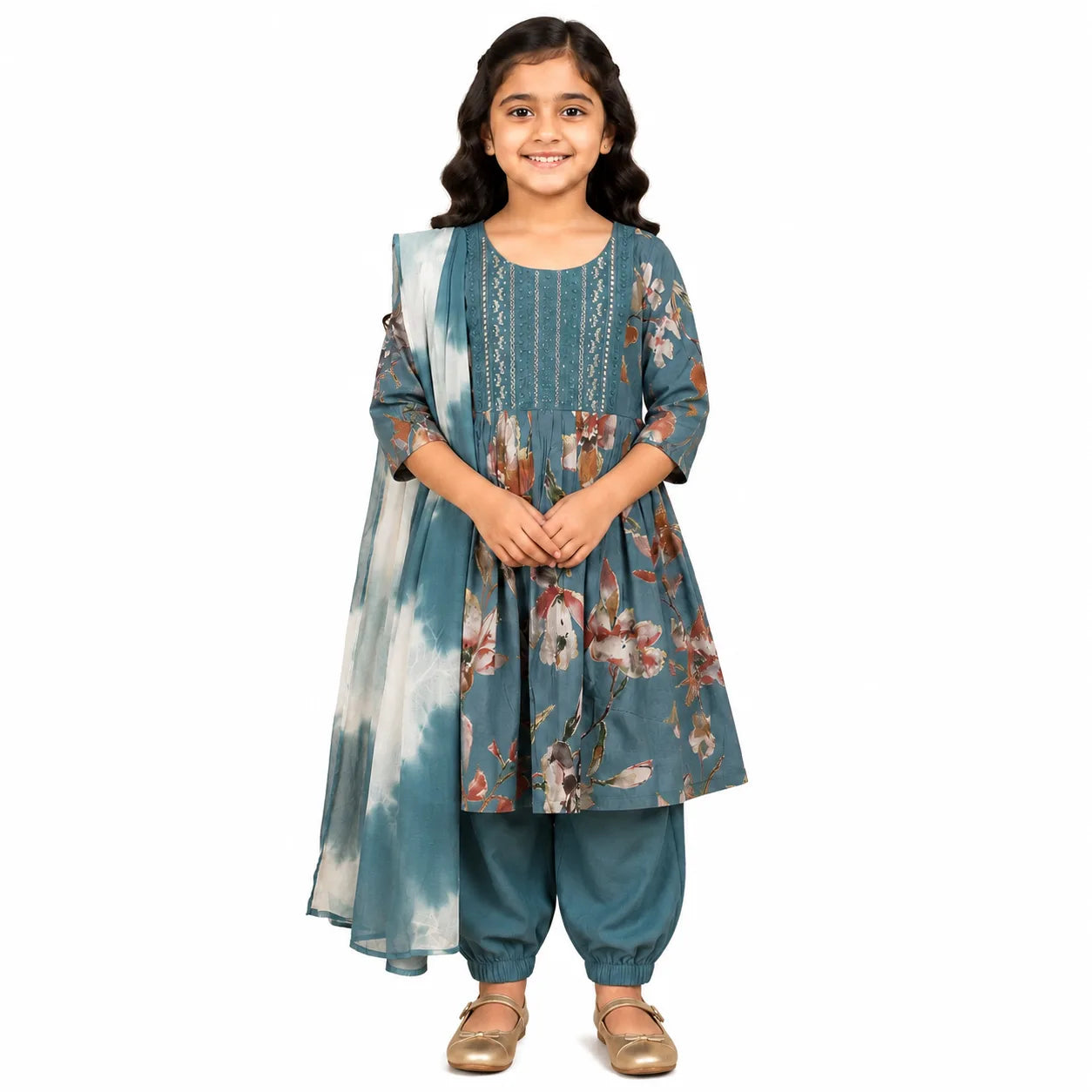 A young girl modeling a traditional three-piece salwar kameez set in teal blue with a floral print and a matching tie-dye dupatta, set against a plain white background.