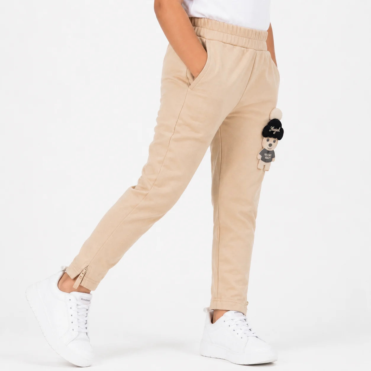 A person wearing beige tapered pants with side pockets, a white t-shirt, and white sneakers, shown from the waist down against a plain white background.