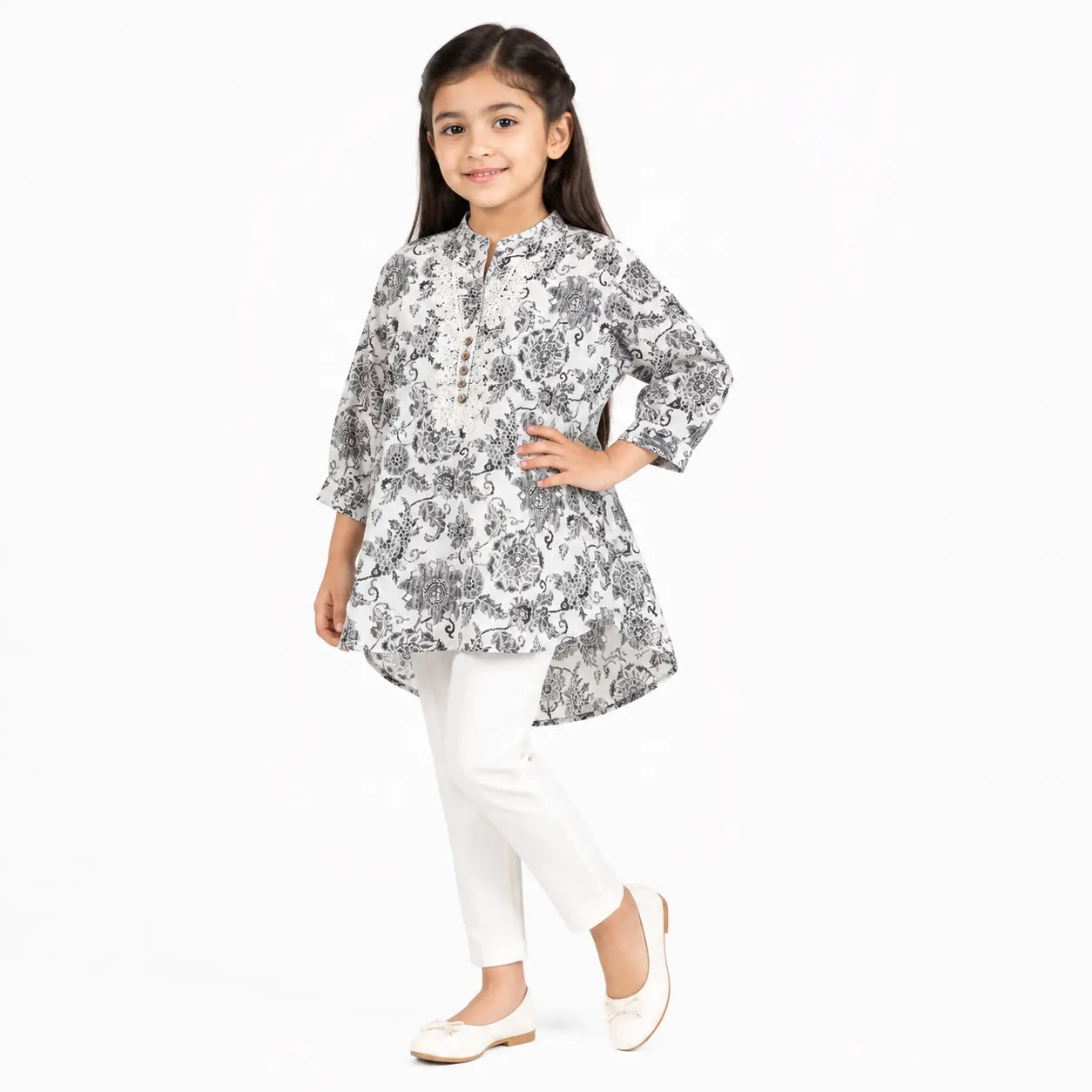 A young girl modeling a white three-quarter sleeve kurta with a black floral print, paired with white trousers and white flat shoes, against a plain white background.