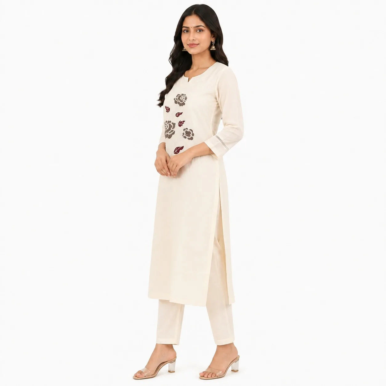 A woman modeling a cream-colored Indian ethnic kurta set with matching pants and clear high-heeled sandals, set against a plain white background.