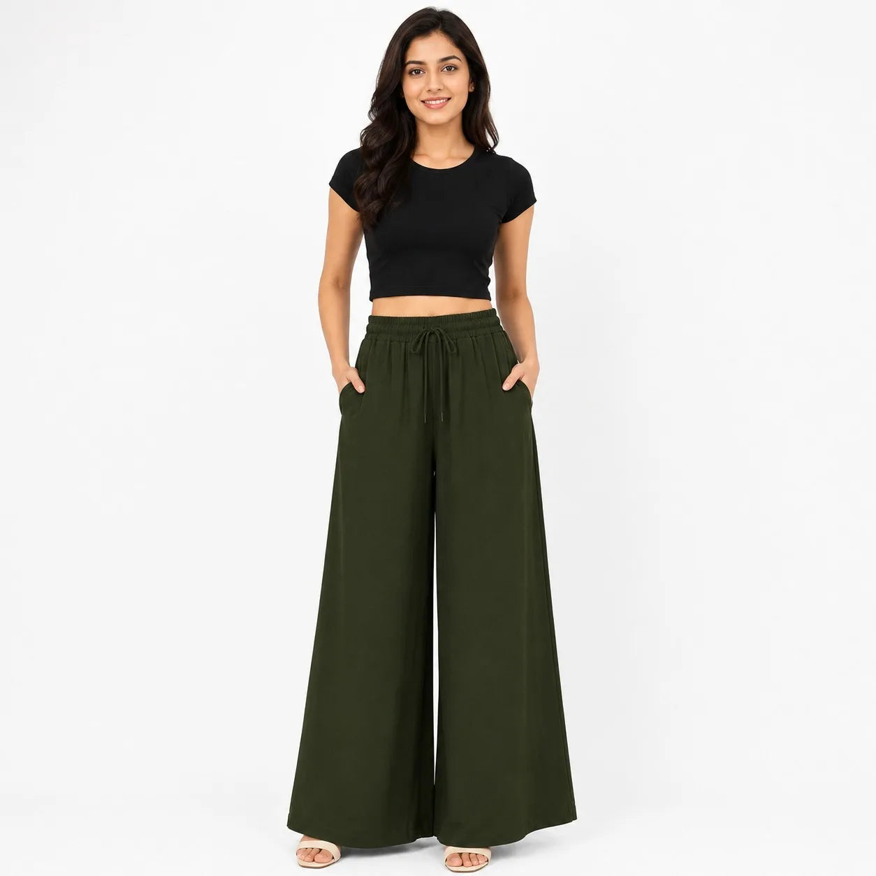 A woman modeling a pair of olive green wide-leg drawstring pants with side pockets, paired with a black crop top, against a plain white studio background.