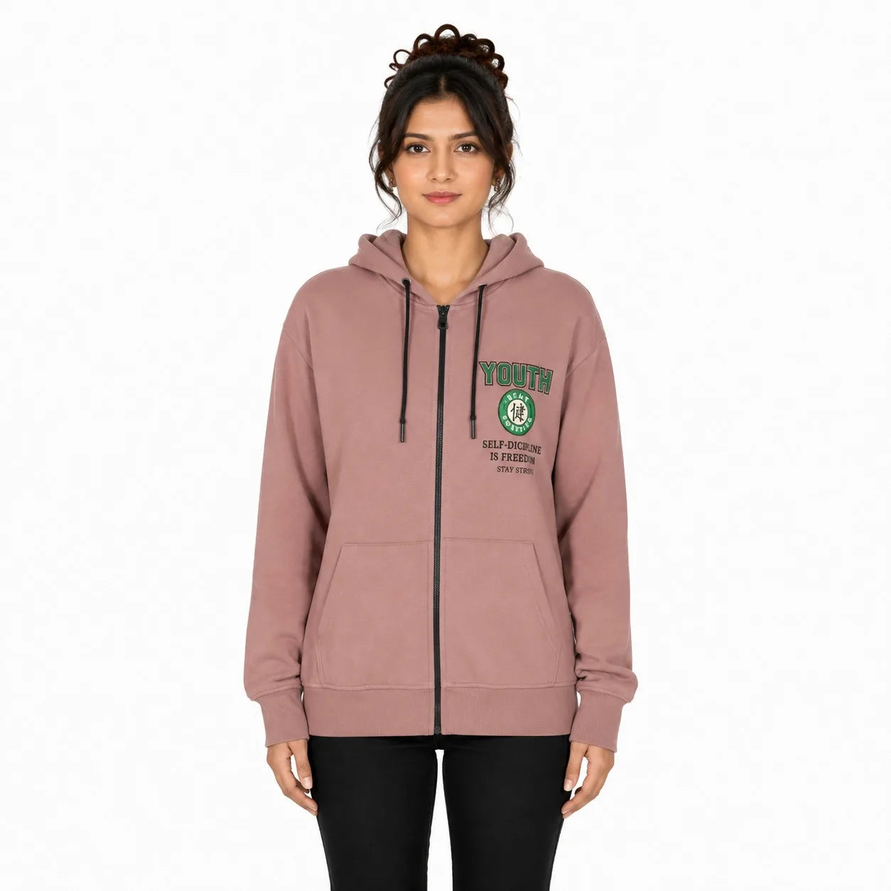 A woman modeling a dusty rose zip-up hoodie with a green and white 'YOUTH' graphic on the left chest, paired with black pants against a plain white background.