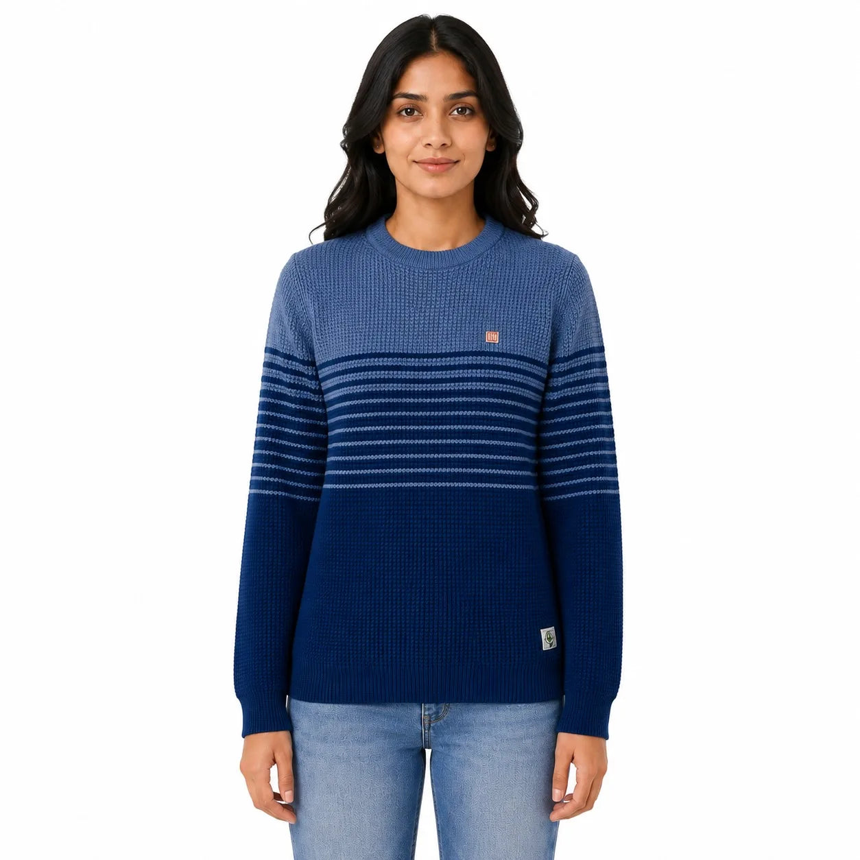 A woman modeling a blue ribbed knit sweater with horizontal stripes across the chest and sleeves, paired with light blue jeans, against a plain white background.