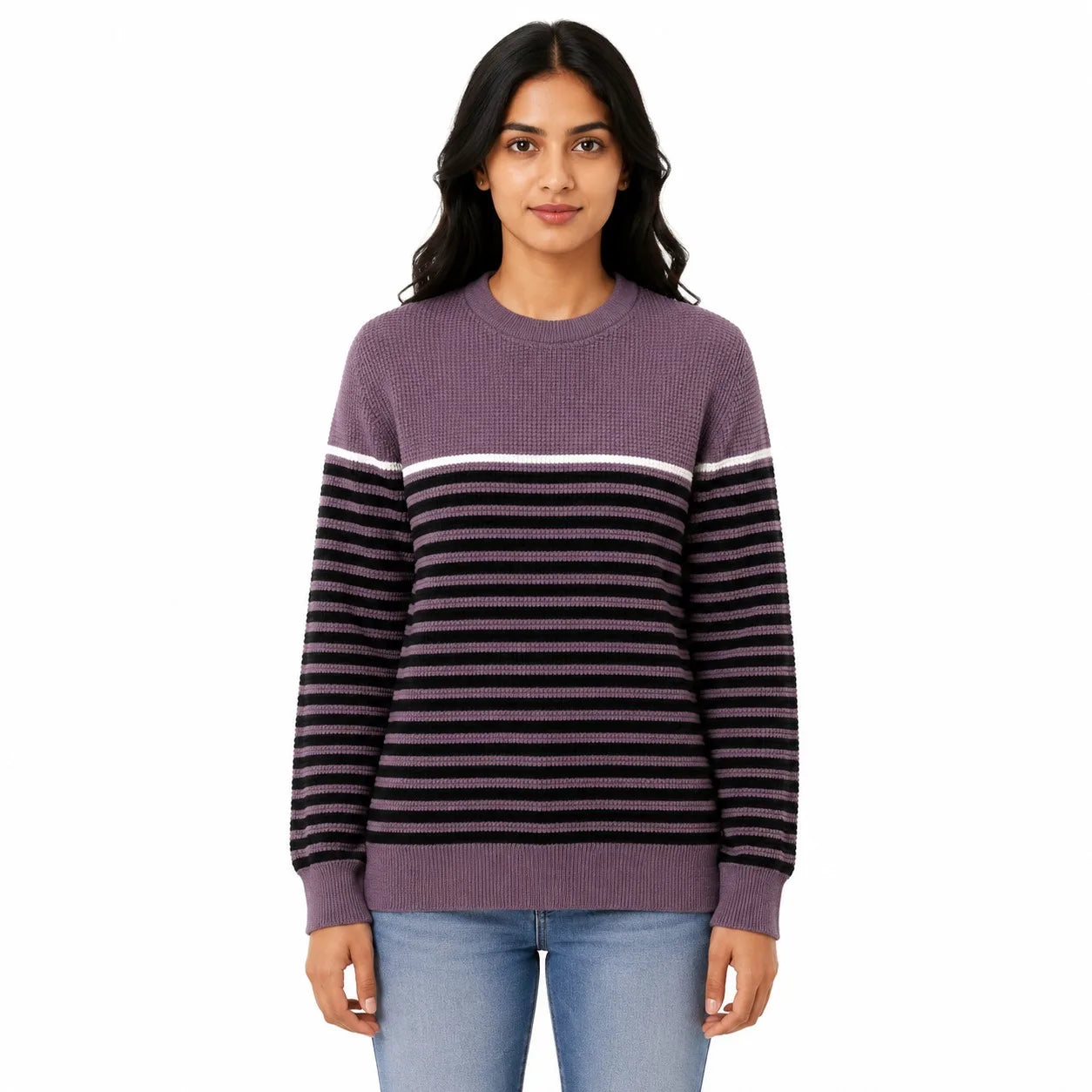 A woman modeling a ribbed knit crewneck sweater with a solid purple upper section and horizontal black and purple stripes across the body and sleeves, paired with light blue jeans against a plain white background.