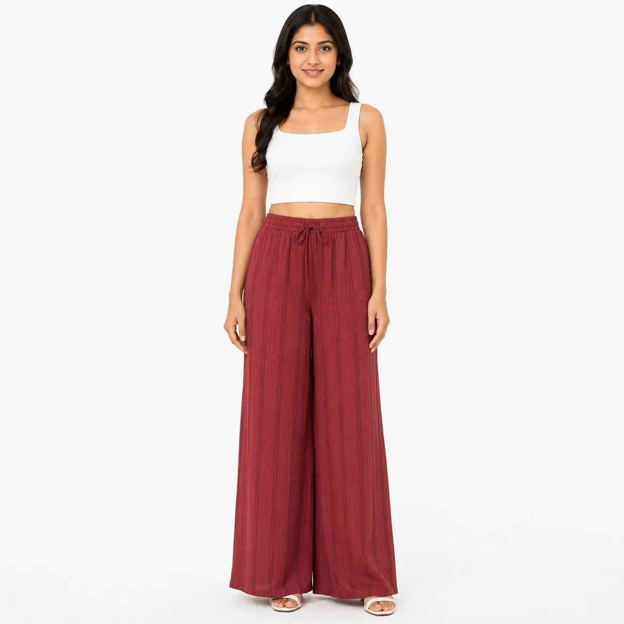 A woman modeling a two-piece outfit consisting of a white sleeveless crop top and high-waisted, wide-leg pleated trousers in a dusty rose or muted red color, set against a plain white studio background.