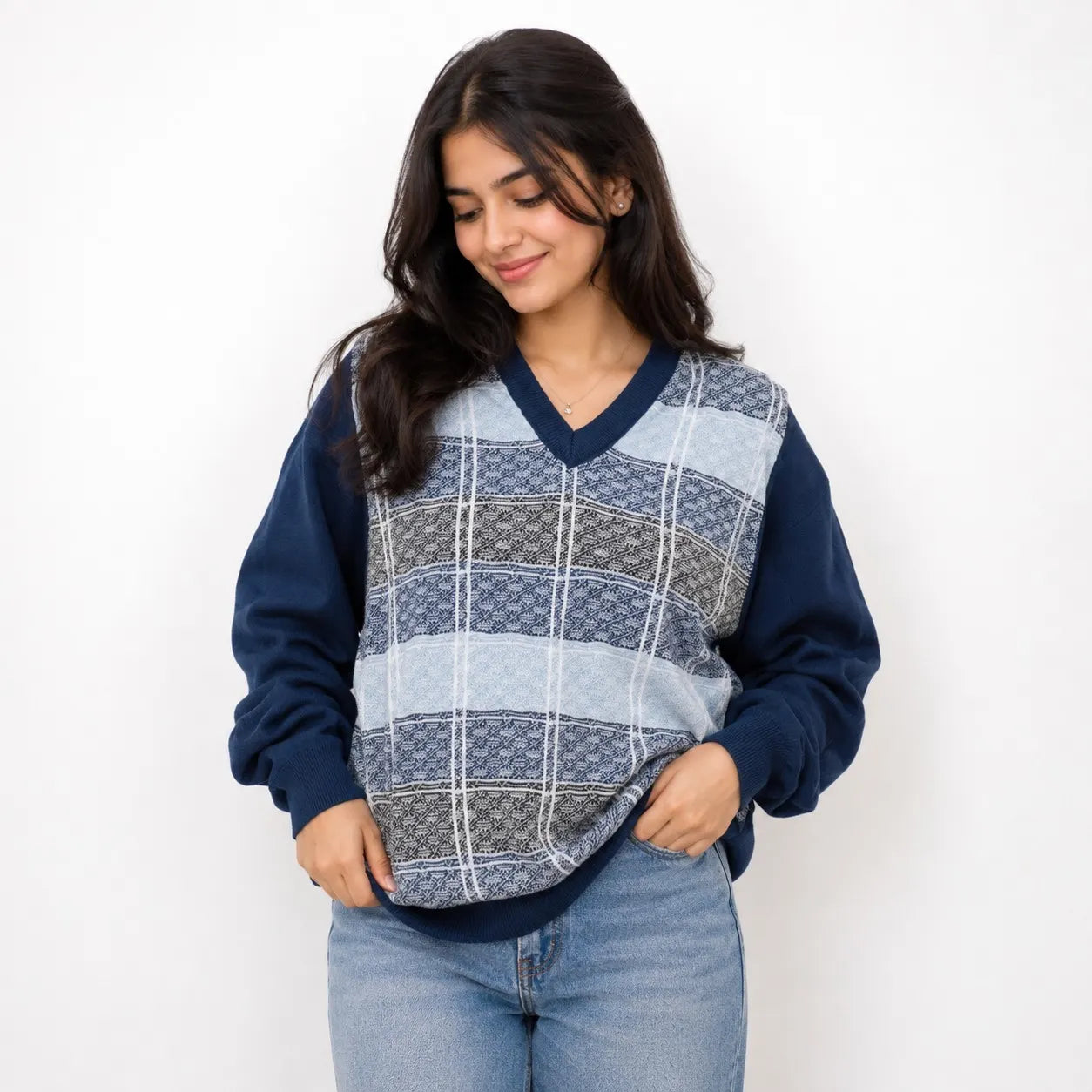 A woman wearing a navy blue long-sleeve sweater vest with a blue, gray, and white plaid patterned front panel, paired with light blue jeans, against a plain white background.