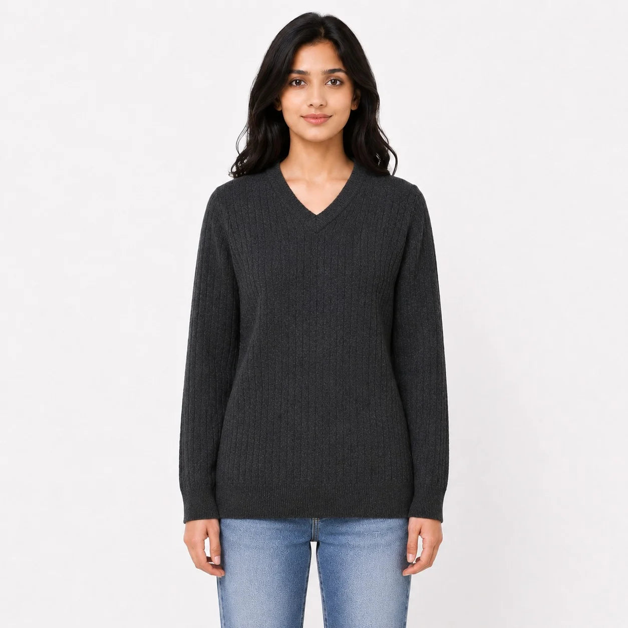 A woman modeling a dark charcoal gray ribbed knit sweater with a V-neck and long sleeves, paired with light blue jeans, against a plain white studio background.