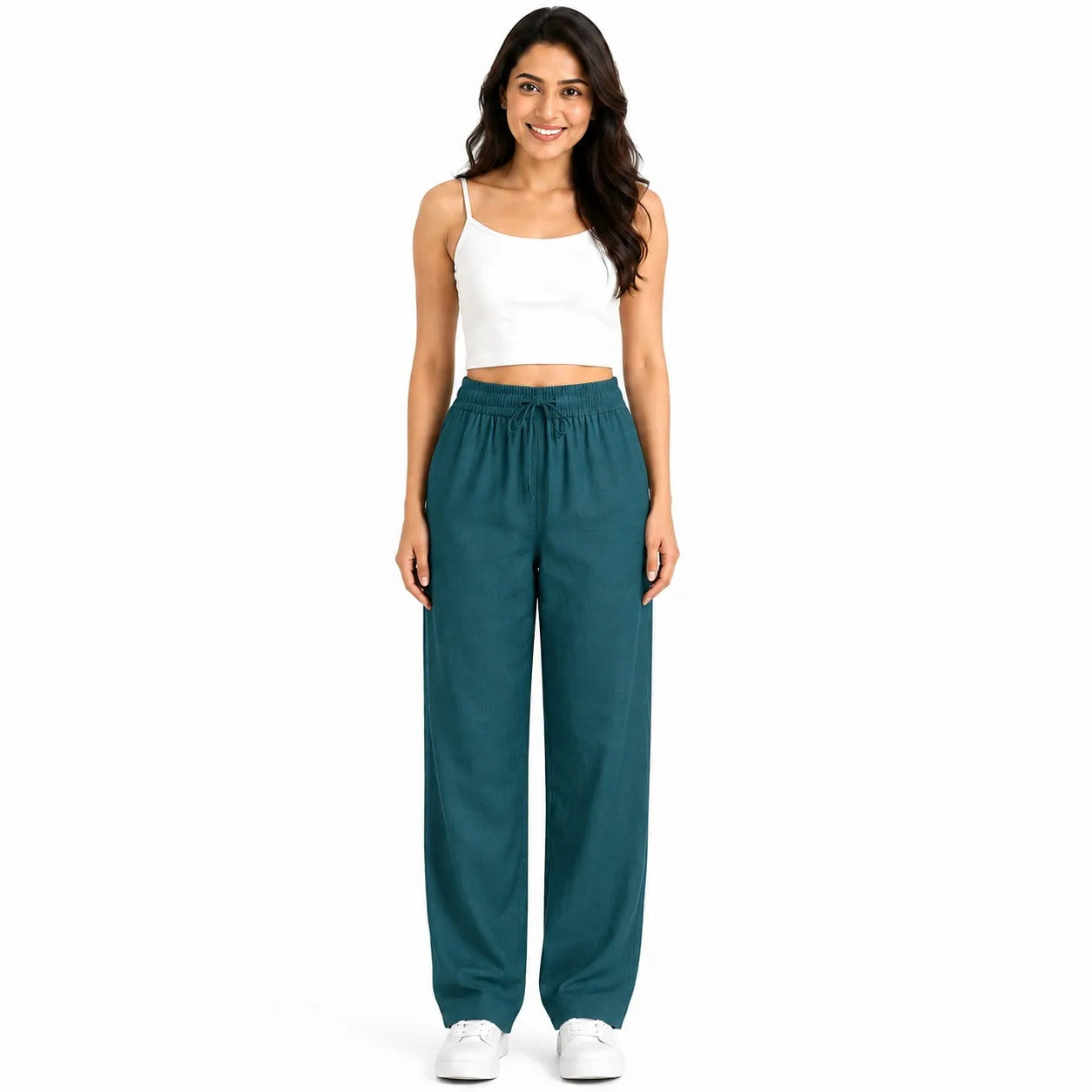A woman modeling a pair of wide-leg teal pants with a drawstring waist, paired with a white crop top and white sneakers, against a plain white background.