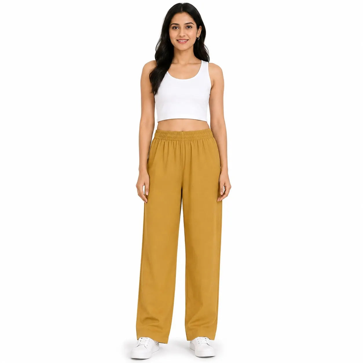 A woman modeling a pair of wide-leg jogger pants in mustard yellow, paired with a white crop top and white sneakers, against a solid white background.