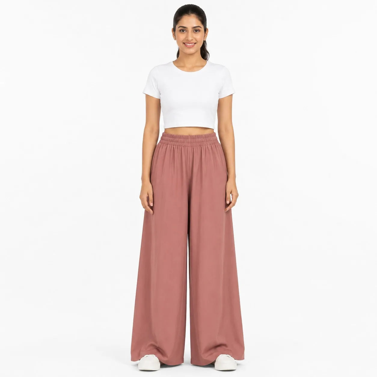 A woman modeling a white short-sleeve crop top and dusty rose wide-leg pants against a plain white studio background.