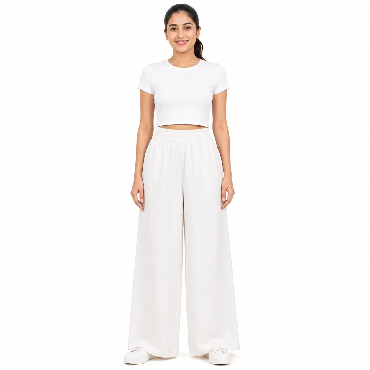 A woman modeling a white two-piece outfit consisting of a short-sleeve crop top and high-waisted wide-leg pants, standing against a solid white background.