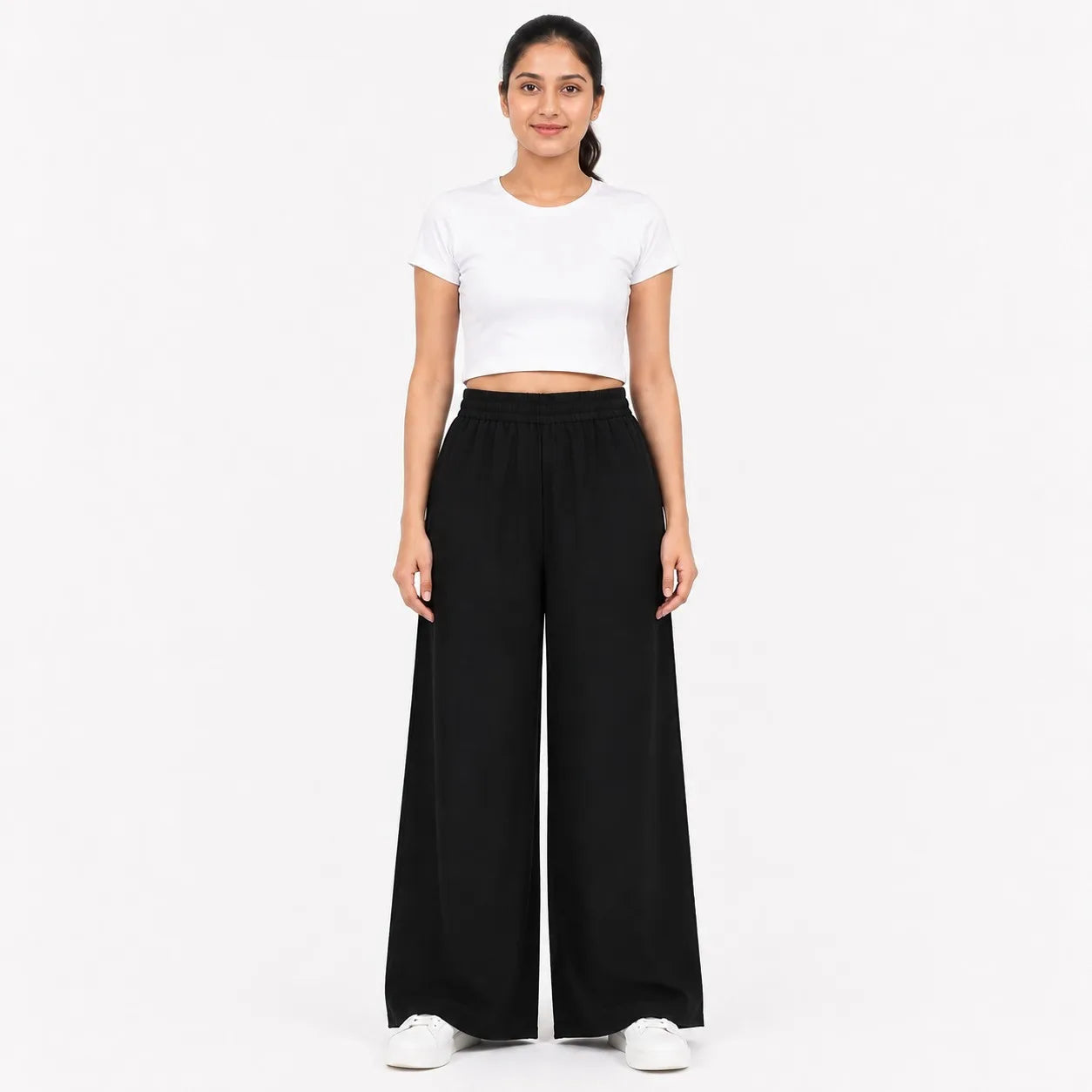A woman modeling a white short-sleeve crop top and black wide-leg pants against a plain white studio background.