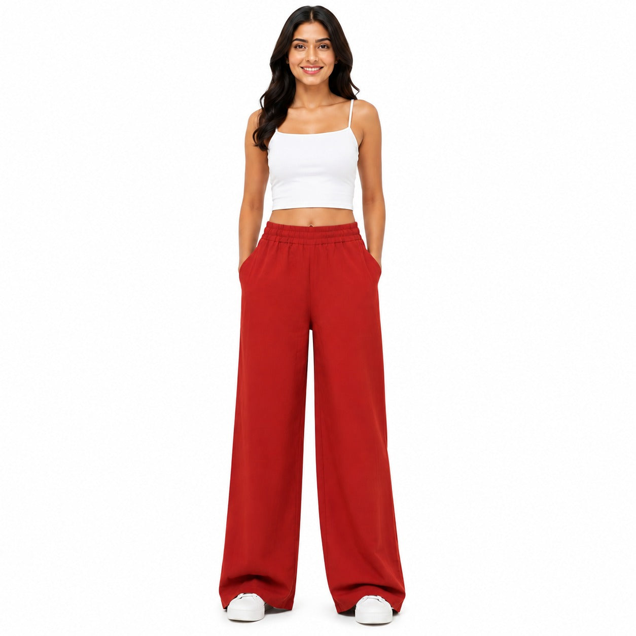 A woman modeling a two-piece outfit consisting of a white spaghetti-strap crop top and high-waisted, wide-leg red pants, standing against a solid white background.