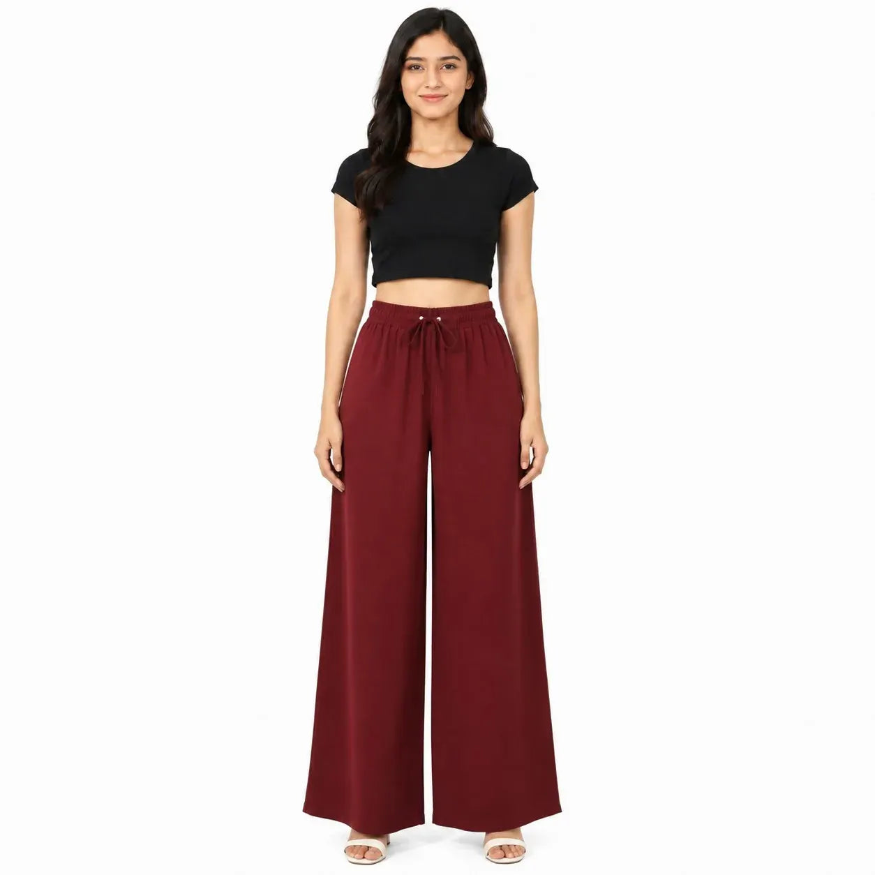 A woman modeling a black short-sleeve crop top and high-waisted, wide-leg burgundy pants against a plain white background.