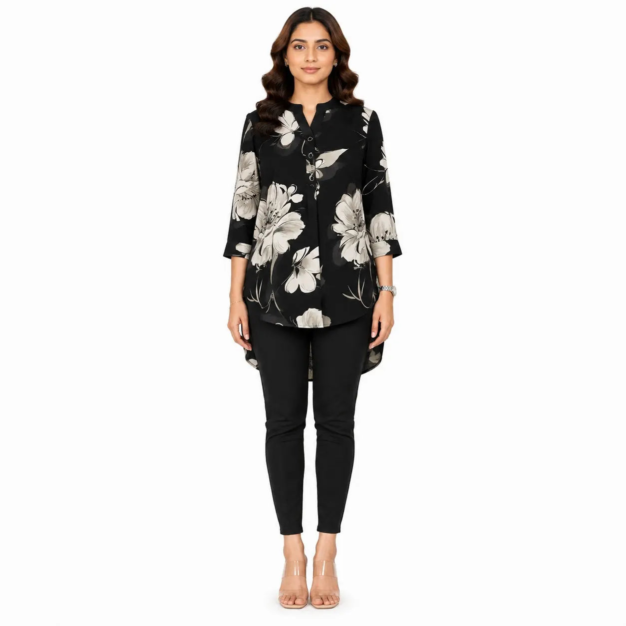 A woman modeling a black three-quarter sleeve button-up blouse with a large white and gray floral print, paired with black skinny pants and clear high-heeled sandals, against a plain white background.