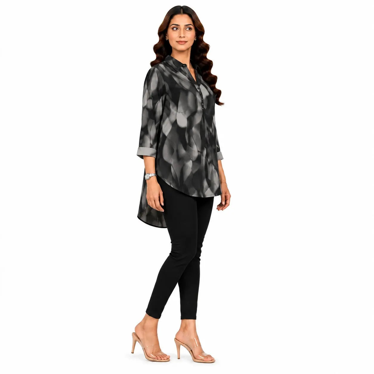 A woman modeling a black and gray abstract patterned long-sleeve tunic top, paired with black pants and clear high-heeled sandals, against a plain white background.