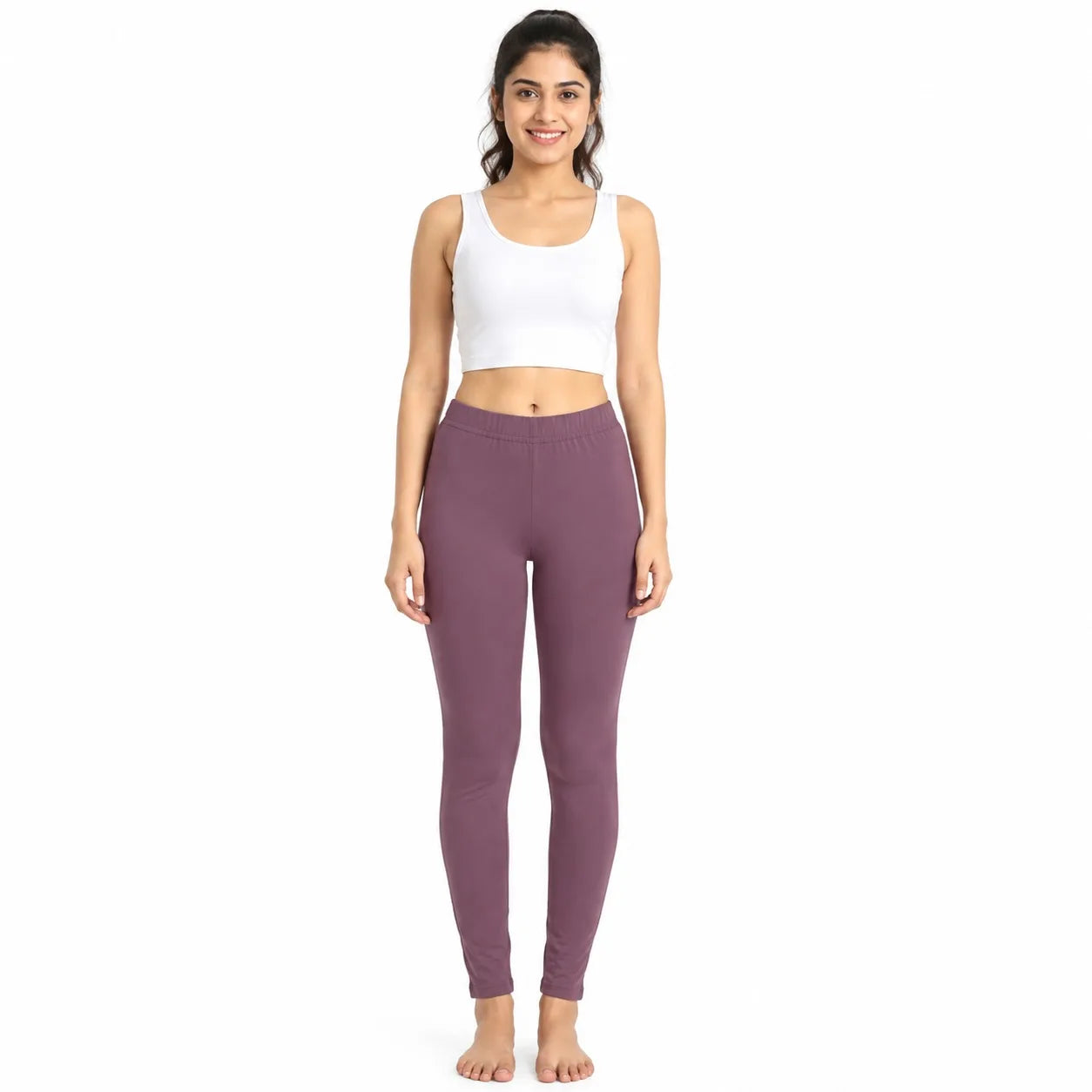 A woman modeling a white ribbed crop tank top and dusty mauve high-waisted leggings against a plain white background.