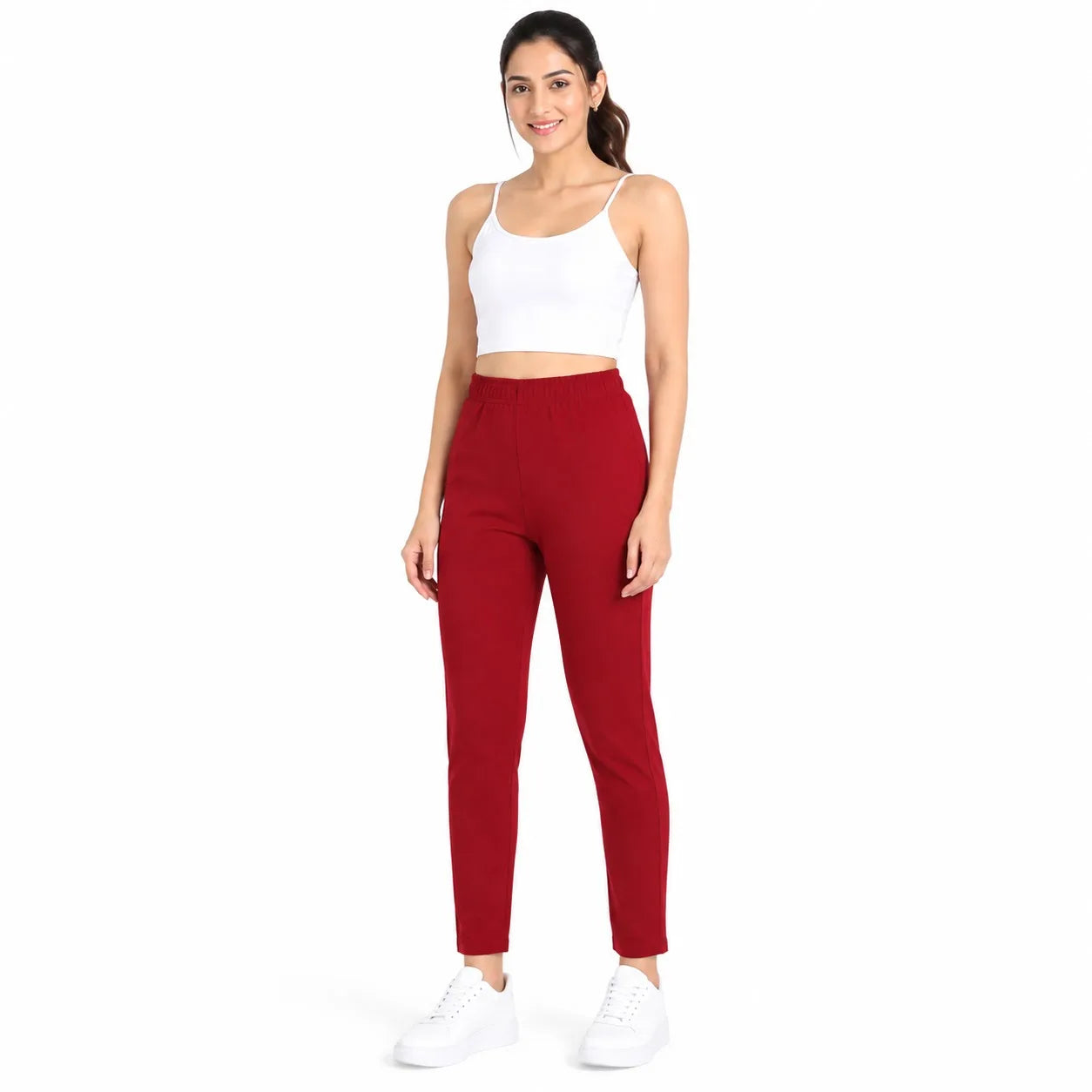 A woman modeling a pair of high-waisted, ankle-length red pants, paired with a white crop top and white sneakers, against a solid white background.