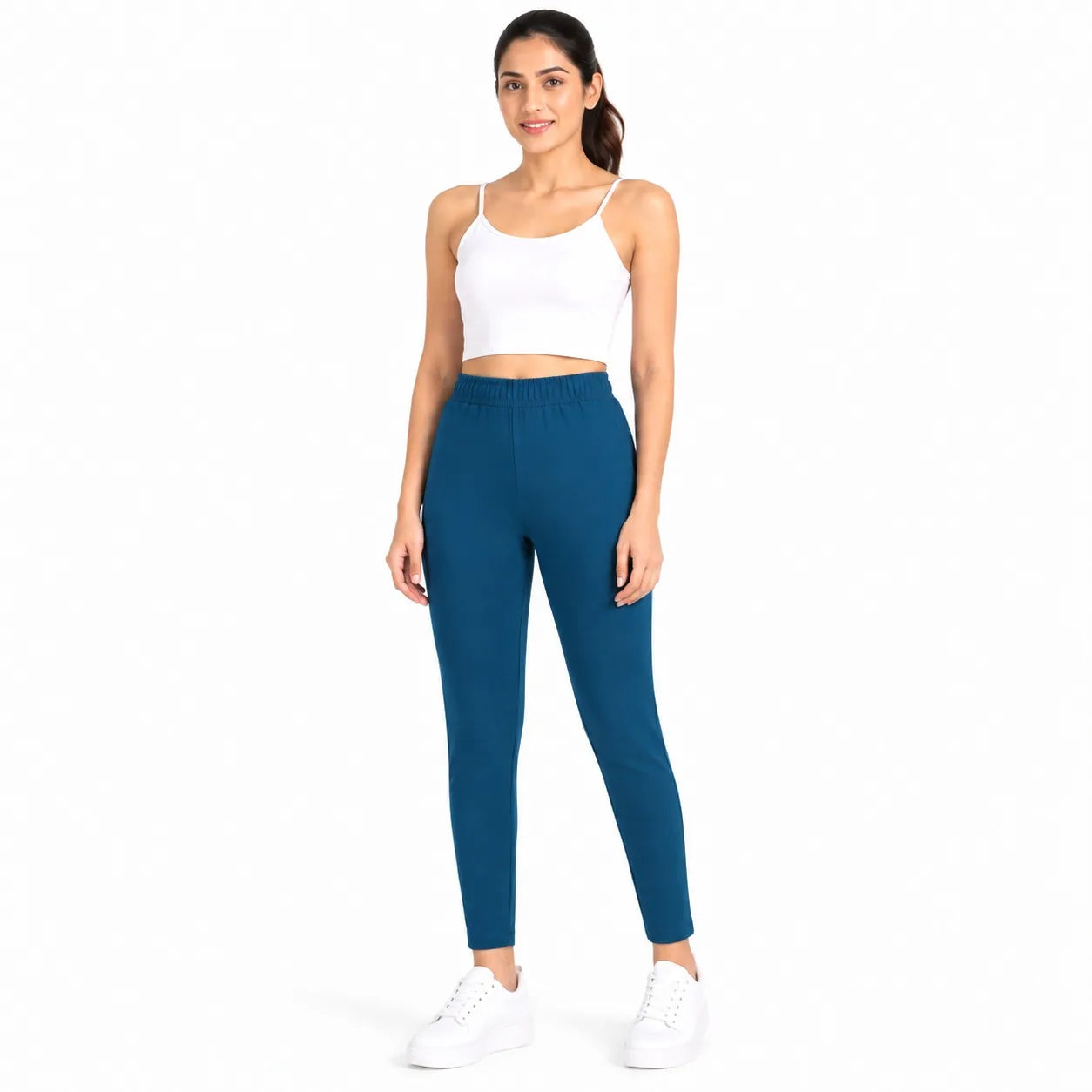 A woman modeling a pair of teal blue athletic leggings with a white crop top and white sneakers against a plain white background.