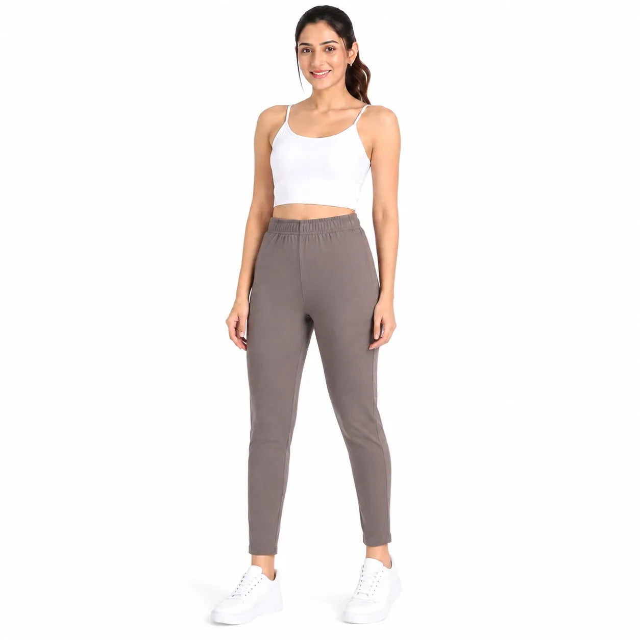 A woman modeling a two-piece activewear set consisting of a white crop tank top and high-waisted, slim-fit gray jogger pants, paired with white sneakers, against a plain white background.