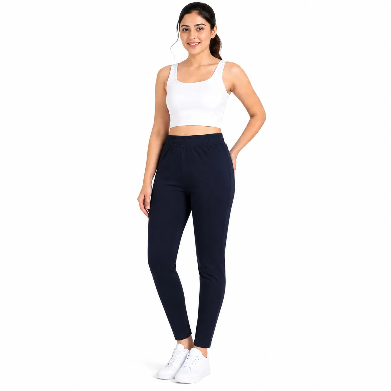 A woman modeling a pair of dark navy blue athletic leggings with a white crop top and white sneakers, standing against a solid white background.