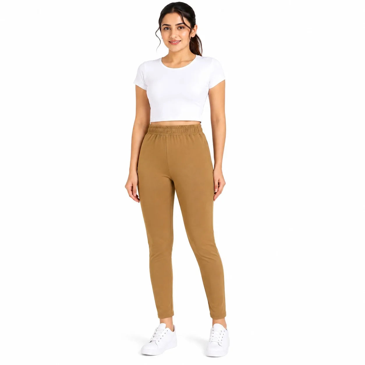 A woman modeling a two-piece activewear set consisting of a white short-sleeve crop top and high-waisted, elastic-waist tan leggings, paired with white sneakers, against a plain white background.