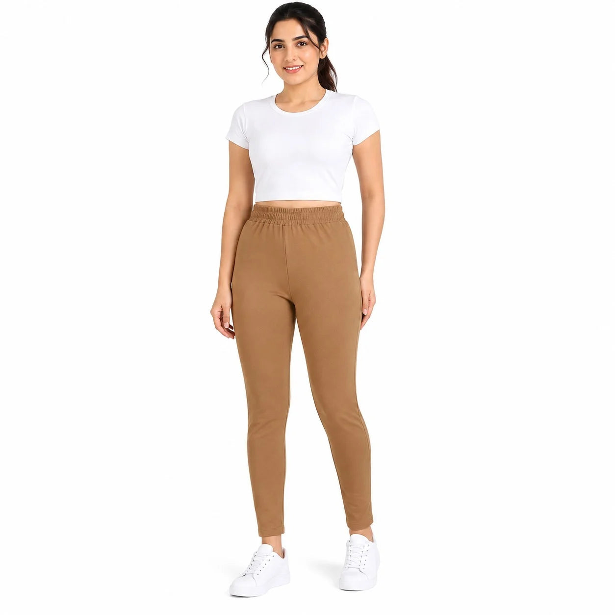 A woman modeling a white short-sleeve crop top and brown fitted leggings with white sneakers, standing against a plain white background.