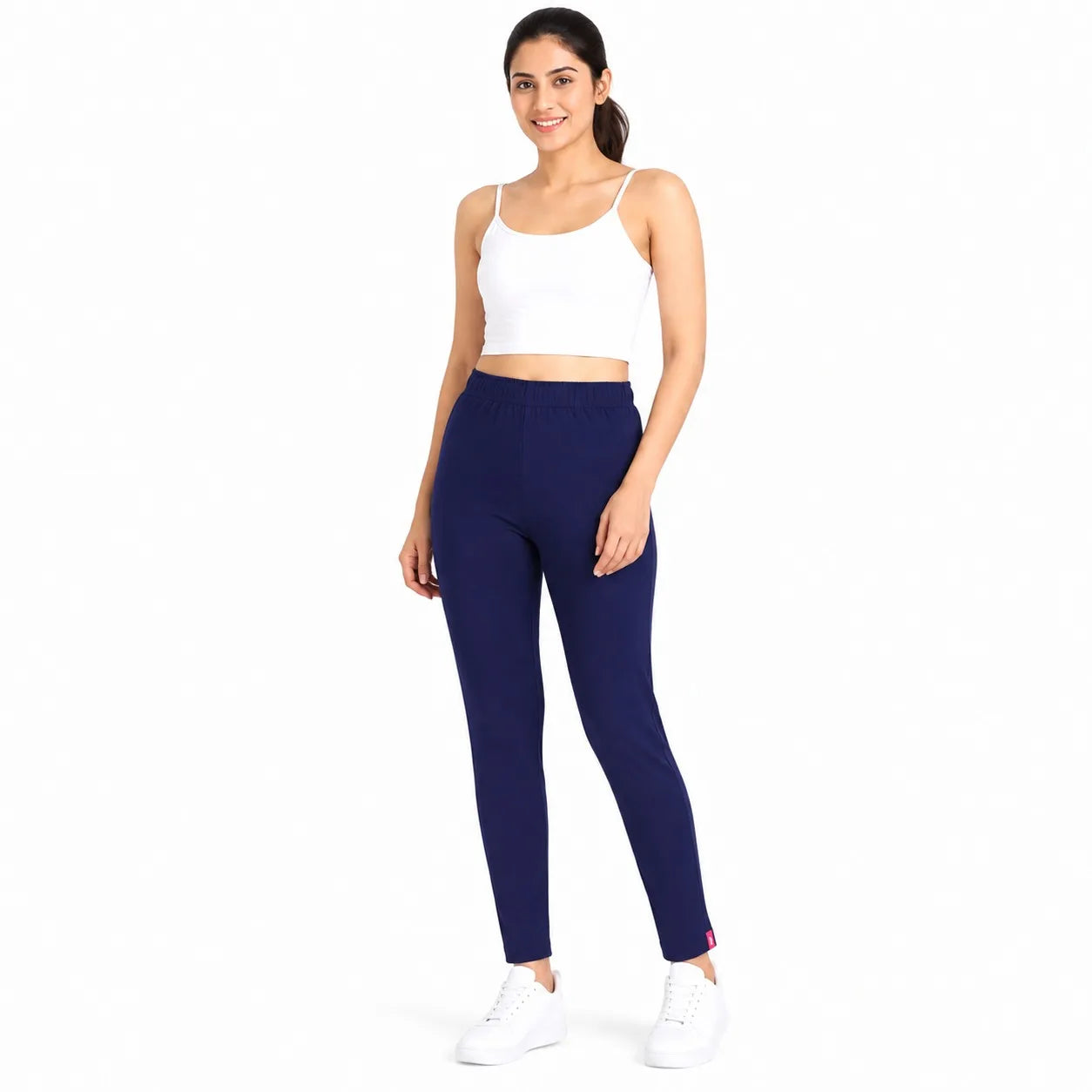 A woman modeling navy blue high-waisted leggings and a white crop top against a solid white background.