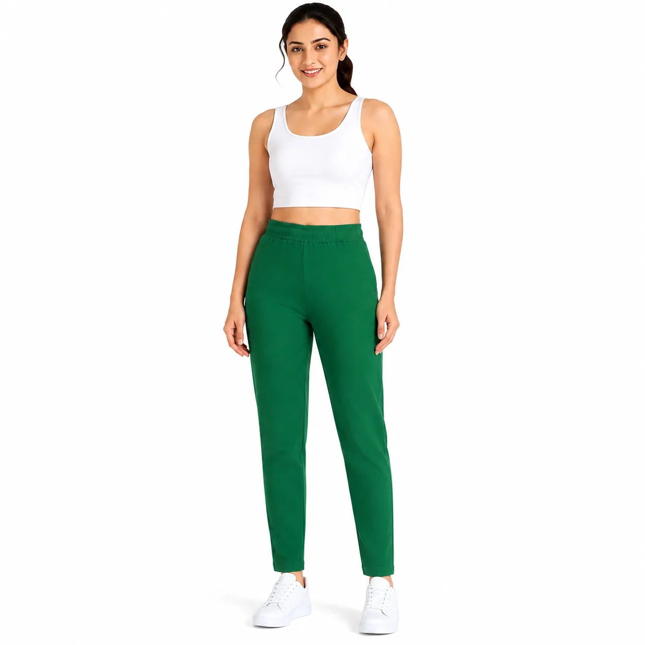 A woman modeling a pair of solid green athletic pants with a white sports bra and white sneakers, standing against a plain white background.