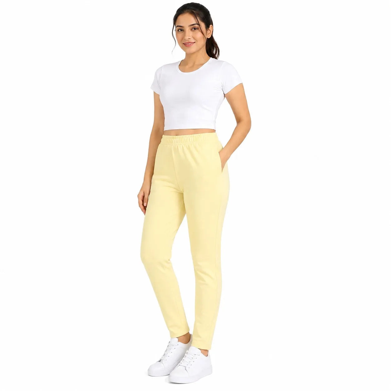A woman modeling a two-piece activewear set consisting of a white short-sleeve crop top and light yellow jogger pants, paired with white sneakers, against a plain white background.