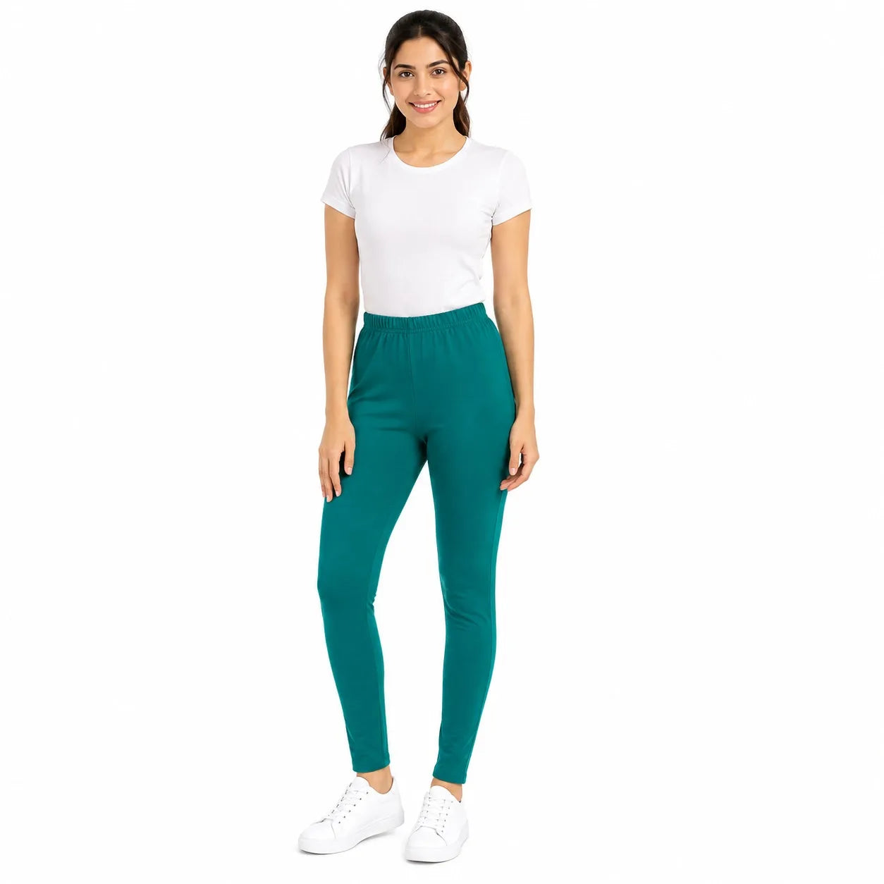 A woman modeling high-waisted, ankle-length teal leggings, paired with a white t-shirt and white sneakers, against a solid white background.