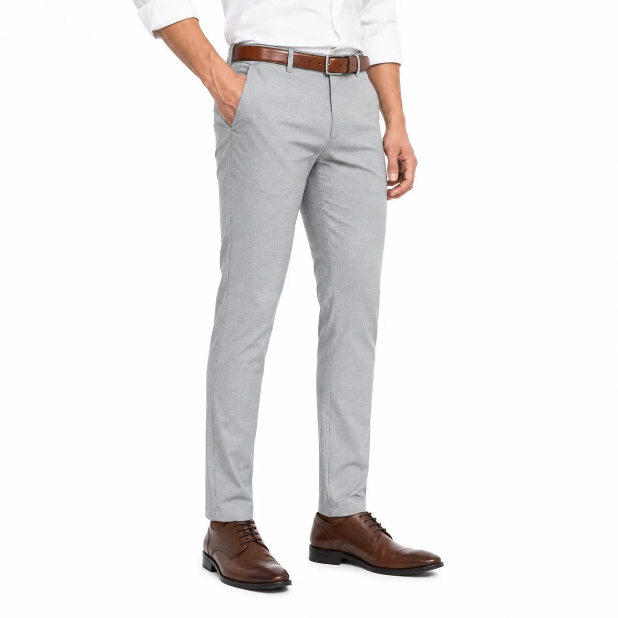 A man wearing light gray slim-fit dress pants, styled with a white shirt, brown leather belt, and brown leather dress shoes, shown from the waist down on a white studio background.
