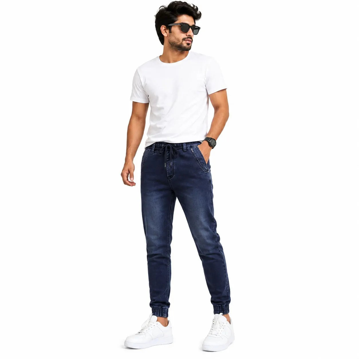 A man modeling dark blue slim-fit jeans with a white t-shirt and white sneakers, standing against a plain white background.