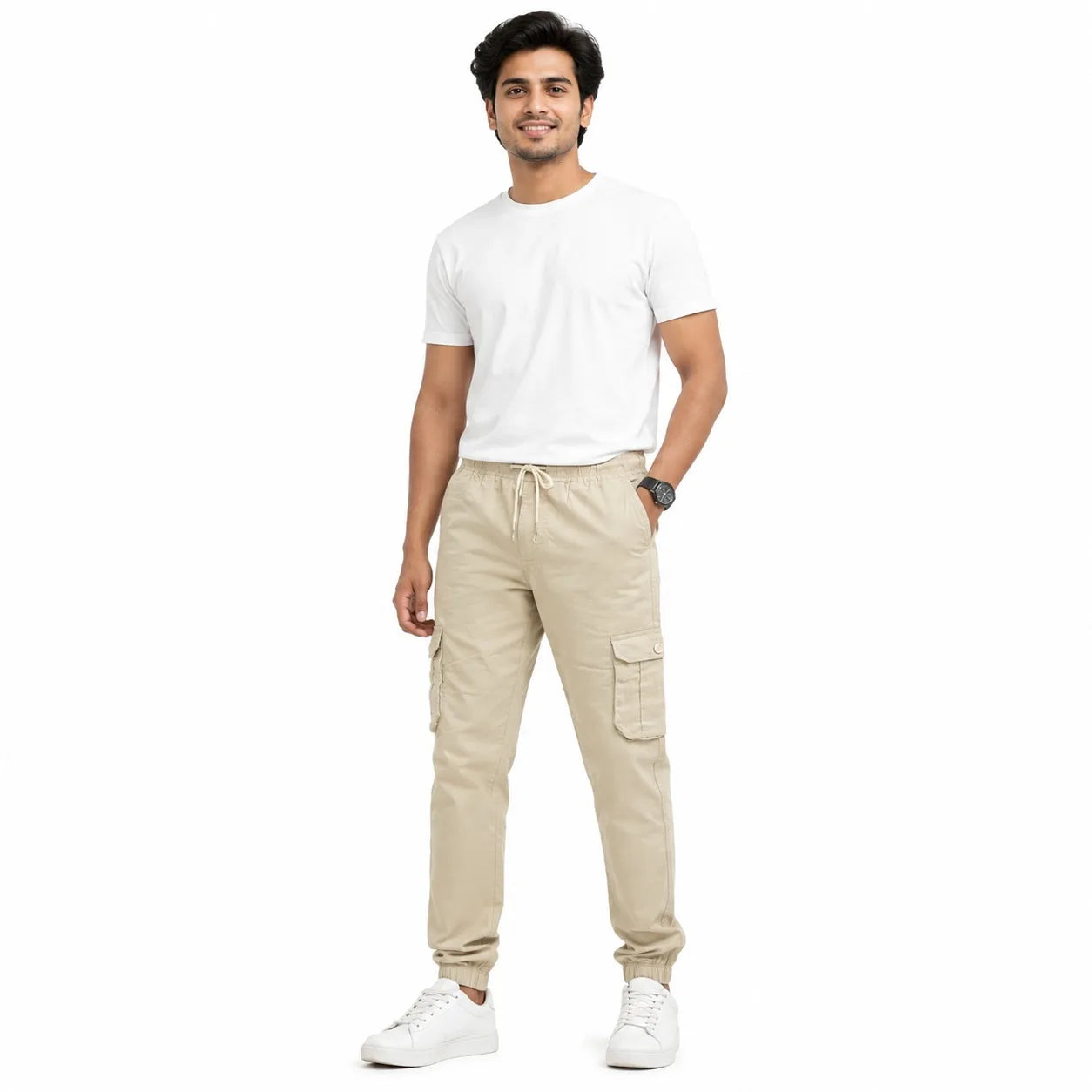 A man modeling beige cargo jogger pants with a white t-shirt and white sneakers against a plain white background.