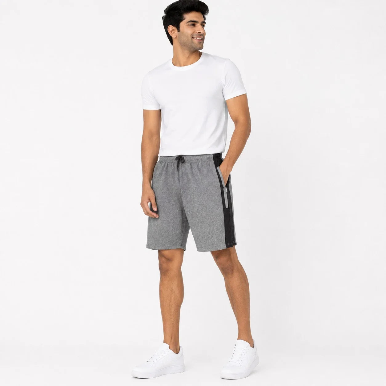 A man modeling gray heathered athletic shorts with a black side stripe and black drawstring, paired with a white t-shirt and white sneakers, against a plain white studio background.