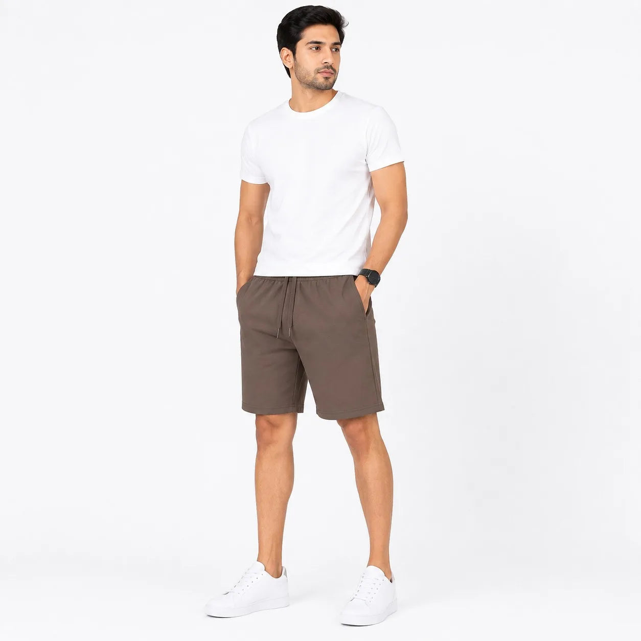 A man modeling a white crew-neck t-shirt and brown drawstring shorts against a plain white studio background.