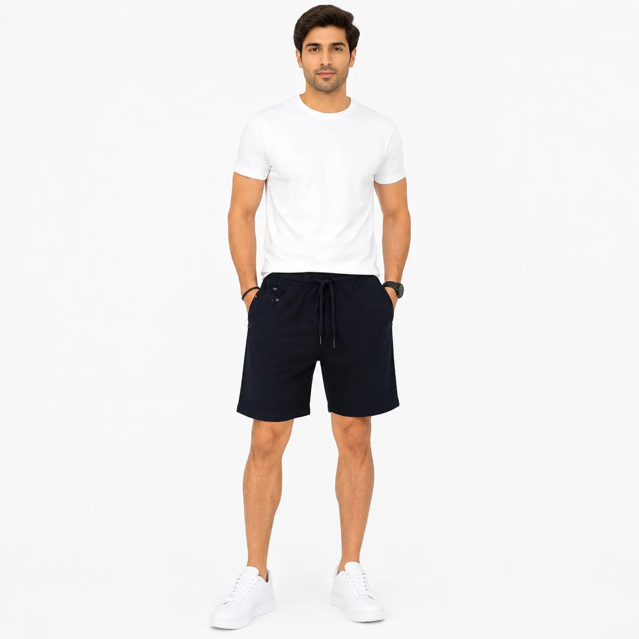 A man modeling a pair of dark navy drawstring shorts, paired with a white t-shirt and white sneakers, standing against a solid white studio background.