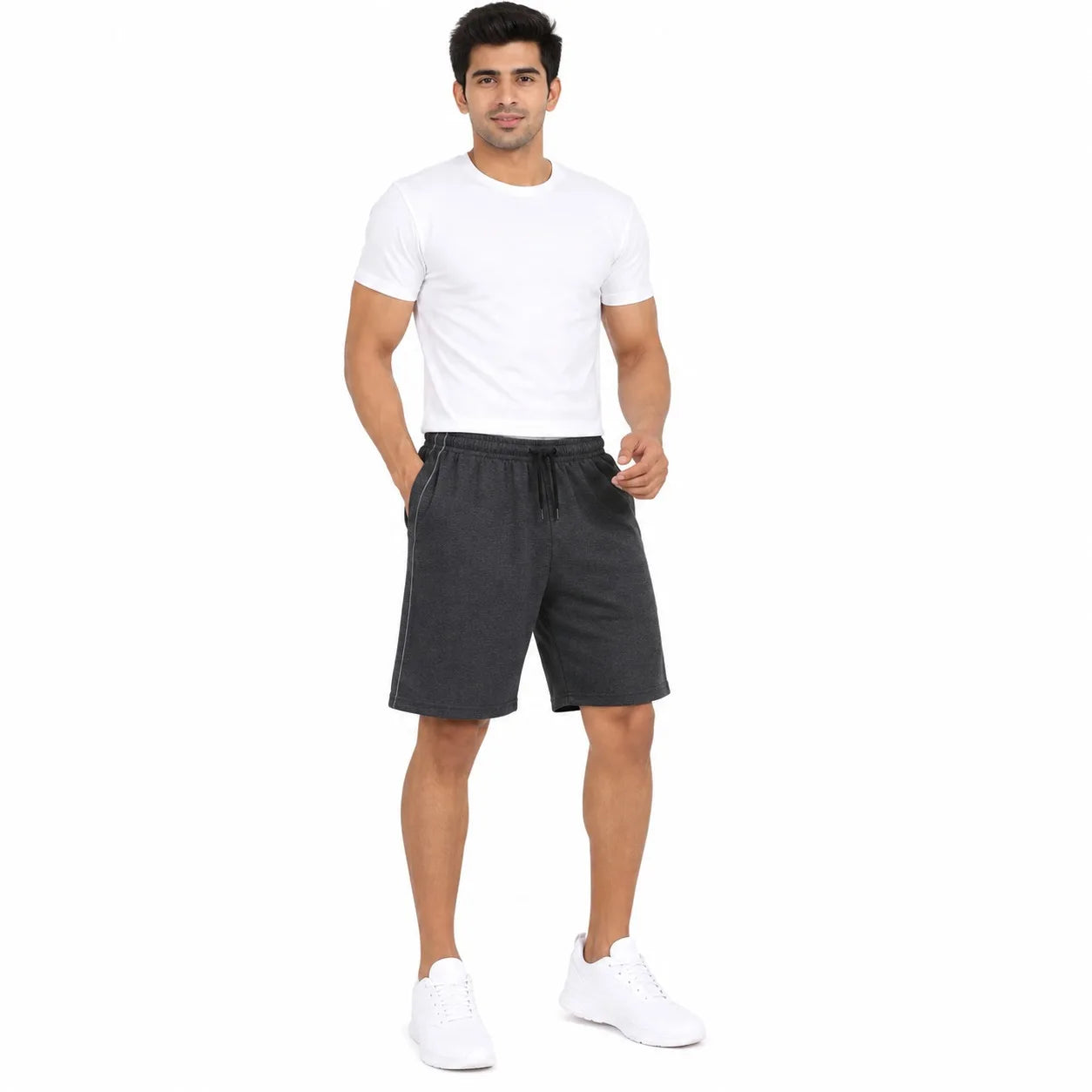 A man modeling dark gray drawstring shorts, paired with a white t-shirt and white sneakers, standing against a solid white background.