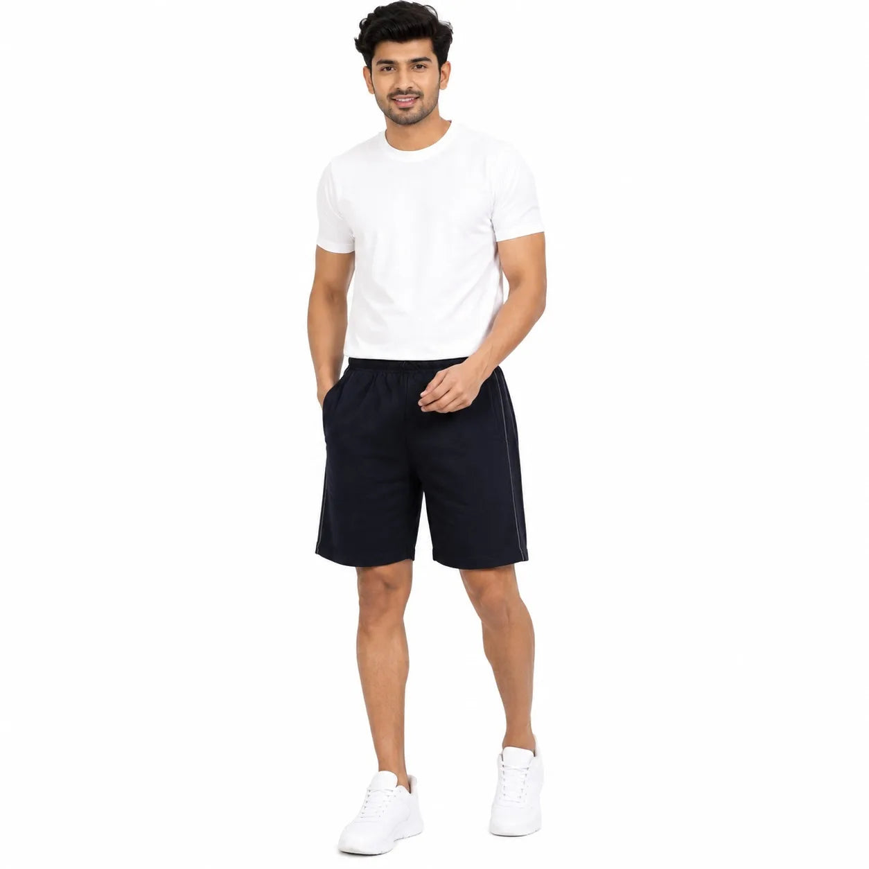 A man modeling a white crew-neck t-shirt and dark navy athletic shorts with white sneakers, set against a plain white background.