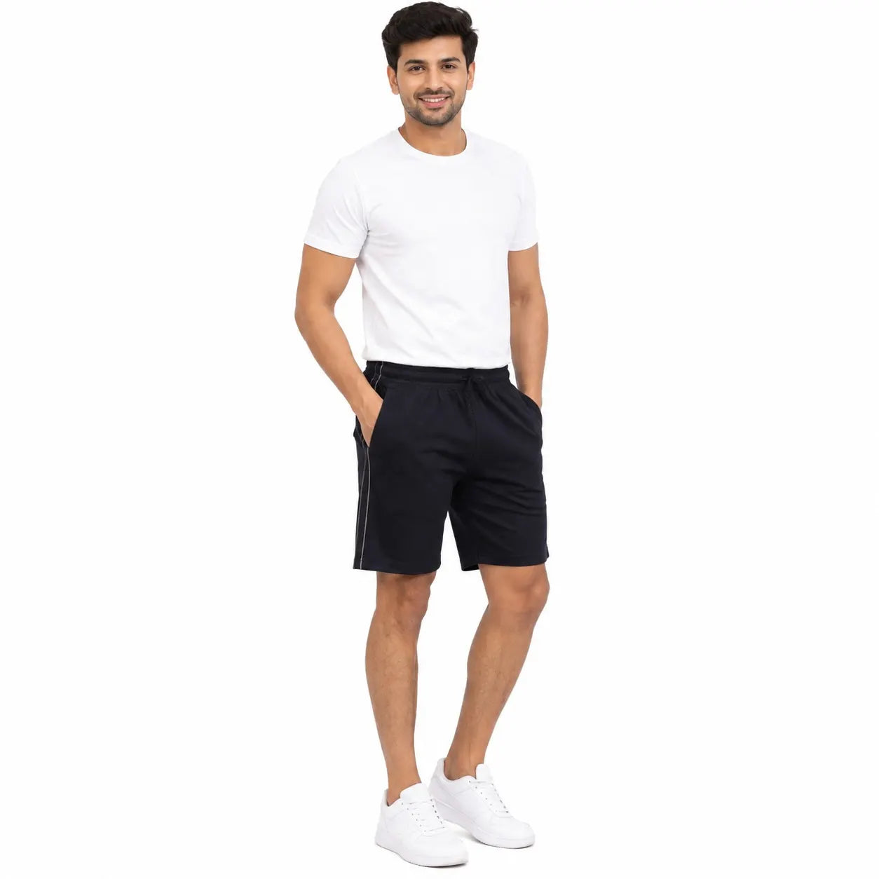 A man modeling a white crew-neck t-shirt and black athletic shorts with white sneakers, standing against a plain white background.