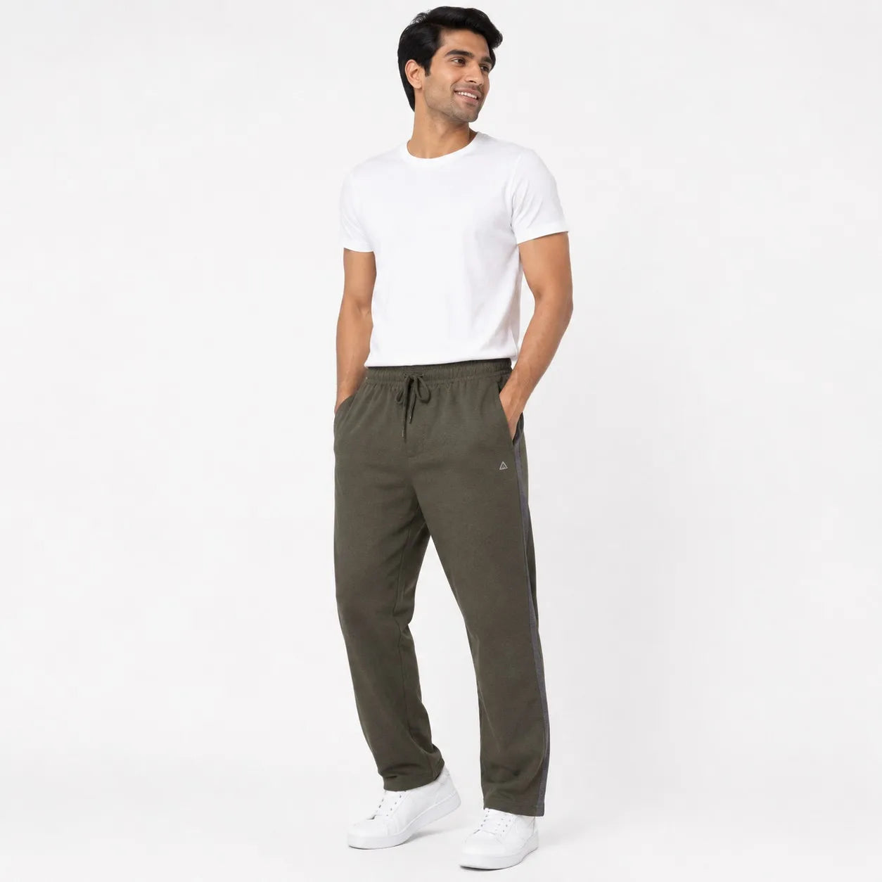 A man wearing olive green drawstring sweatpants, a white t-shirt, and white sneakers, standing against a plain white studio background.