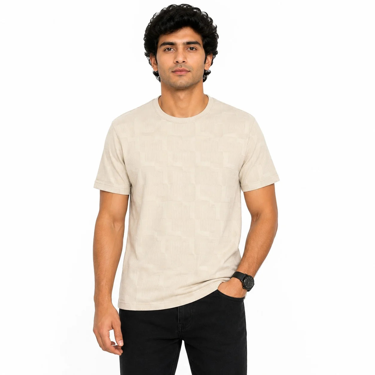 A man wearing a light beige crew-neck t-shirt with a subtle geometric pattern, paired with black pants, standing against a plain white background.