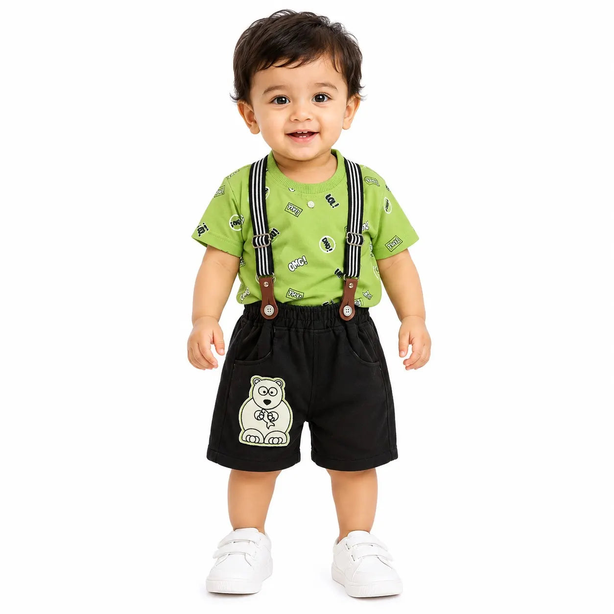 A toddler standing against a white background, wearing a bright green short-sleeve t-shirt with small printed motifs, black suspenders with brown straps, black shorts with a white polar bear graphic, and white sneakers.