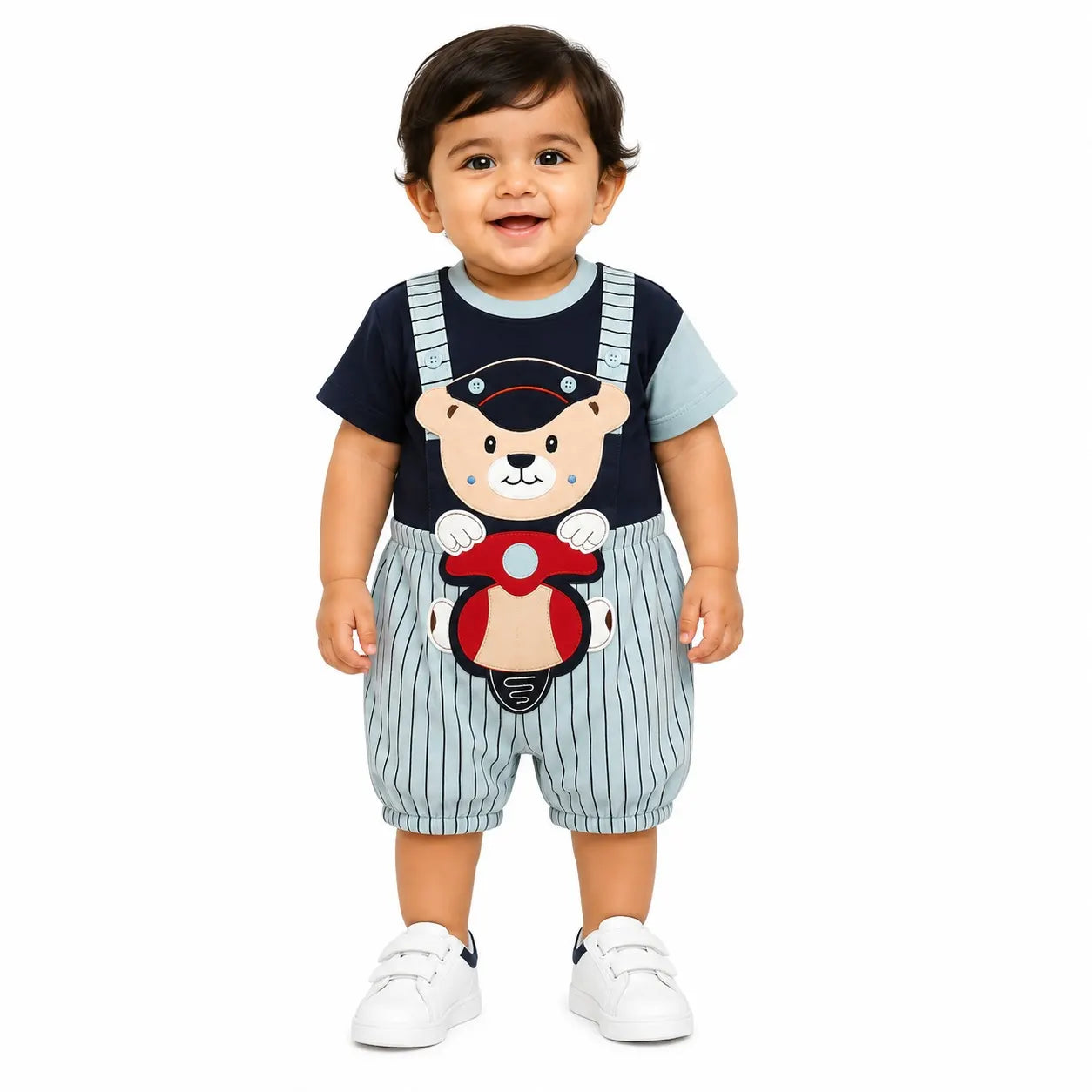 A baby boy wearing a short-sleeve romper with pinstriped overalls and a navy blue graphic shirt featuring a teddy bear driving a red motorcycle, standing against a white background.