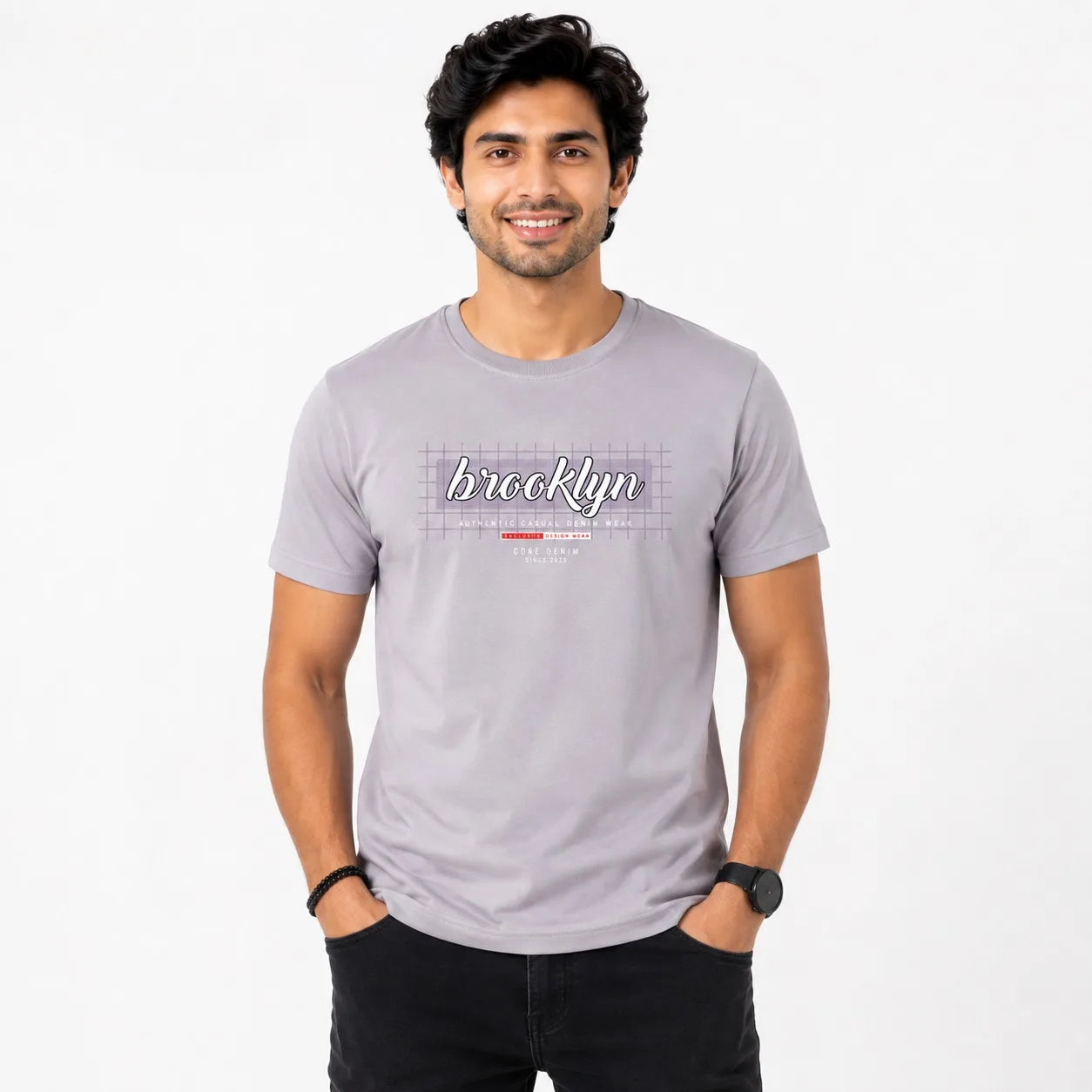 A man wearing a light gray crewneck t-shirt with a 'Brooklyn' graphic on the chest, paired with black pants, standing against a plain white background.